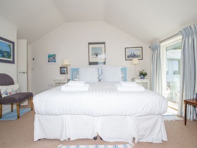 A bedroom with a large bed two bedside tables lamps chair and framed pictures at Curlew House in Cosheston