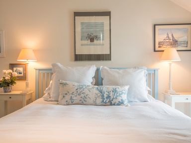 A bedroom with a bed with white and blue pillows two bedside tables with lamps and framed pictures on the wall at Curlew House in Cosheston