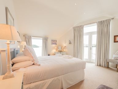 A bedroom with a bed lamps curtains and a chair at Curlew House in Cosheston