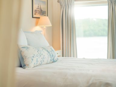 A bedroom with a bed pillows a lamp a framed picture and a window with curtains at Curlew House in Cosheston