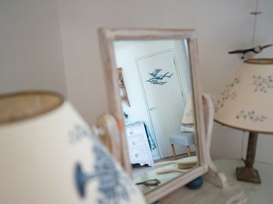 A mirror on a table reflecting a door with bird decorations and a chair at Curlew House in Cosheston