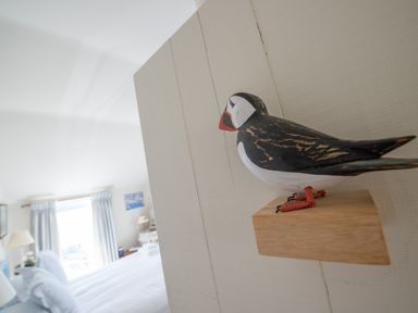 A close up of a wooden puffin decoration mounted on a white wall facing a bedroom with a bed and window at Curlew House in Cosheston