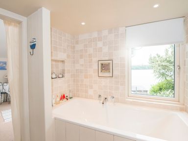 A bathroom with a bathtub beige tiled walls and a window showing greenery outside at Curlew House in Cosheston