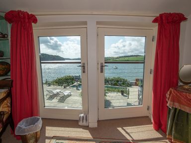 A room with double glass doors overlooking a patio with lounge chairs and a body of water at Curlew House in Cosheston
