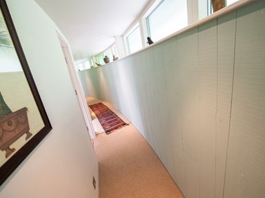 A narrow curved hallway with a colorful runner rug and windows along one side at Curlew House in Cosheston