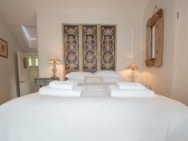 A bedroom with a bed made with white linens and towels a decorative headboard two bedside tables with lamps and a wooden framed mirror on the wall at Curlew House in Cosheston