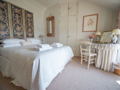 A bedroom with a bed and folded towels a wooden chair and a dressing table with lamps and flowers at Curlew House in Cosheston