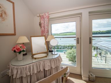 A dressing table with mirrors lamps and flowers near glass doors overlooking a lake at Curlew House in Cosheston
