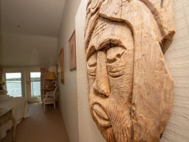 A wooden carved face wall decoration in a bedroom with a chair lamp and ocean view at Curlew House in Cosheston