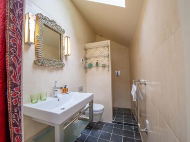 A bathroom with a white sink and mirror with lights a towel rack and a shower area at Curlew House in Cosheston