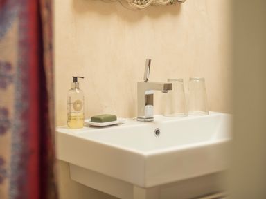 A bathroom sink with a soap dispenser green soap on a dish two glasses and a faucet at Curlew House in Cosheston