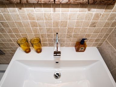 A bathroom sink with a modern faucet two amber glasses and a soap dispenser on a tiled backsplash at Curlew House in Cosheston