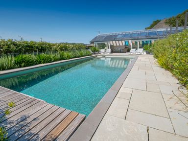 An outdoor swimming pool with lounge chairs and a glass covered seating area at Curlew House in Cosheston