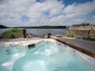 A hot tub on a wooden deck overlooking a lake with hills and boats in the distance at Curlew House in Cosheston