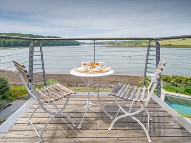 A wooden deck with two chairs and a small round table with breakfast near a river at Curlew House in Cosheston