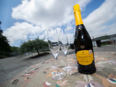 A bottle of prosecco and two empty champagne glasses on a decorated stone table outdoors at Curlew House in Cosheston