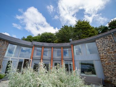 Exterior view of a curved house with large windows and orange pillars surrounded by greenery at Curlew House in Cosheston