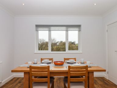 A dining room with a wooden table set for four and a window showing trees outside at West View in Northlew near Hatherleigh