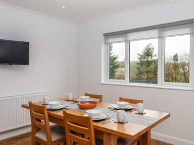 A dining room with a wooden table set for four near a window in West View Northlew near Hatherleigh