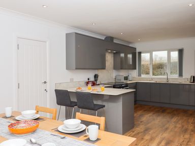 A kitchen with grey cabinets a wooden dining table and chairs and a window with a view at West View in Northlew near Hatherleigh