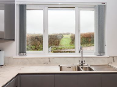 A kitchen sink under a window with grey vertical blinds and marble countertops at West View in Northlew near Hatherleigh
