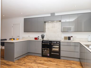 A modern kitchen with grey cabinets a black stove a microwave and a wooden floor at West View Northlew near Hatherleigh