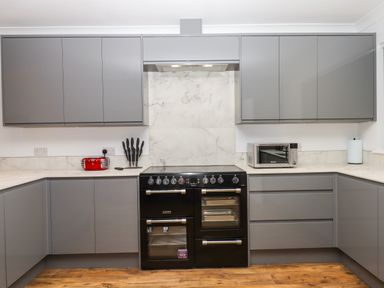 A modern kitchen with grey cabinets a black stove a red toaster a microwave and knives on the counter at West View Northlew near Hatherleigh