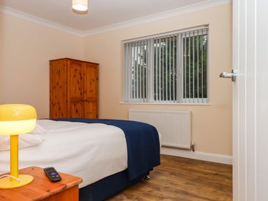 A bedroom with a bed a wooden wardrobe a bedside table with a yellow lamp and a remote control at West View in Northlew near Hatherleigh