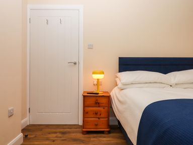 A bedroom with a bed side table holding a lamp and remote near a closed door at West View in Northlew near Hatherleigh