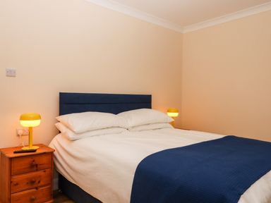 A bedroom with a double bed with blue headboard white bedding and blue throw and wooden nightstands with yellow lamps at West View in Northlew near Hatherleigh
