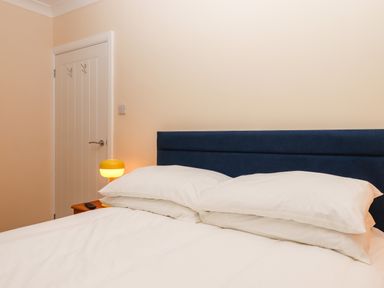 A bedroom with a white bed and pillows and a blue headboard with a yellow lamp on a wooden nightstand at West View in Northlew near Hatherleigh