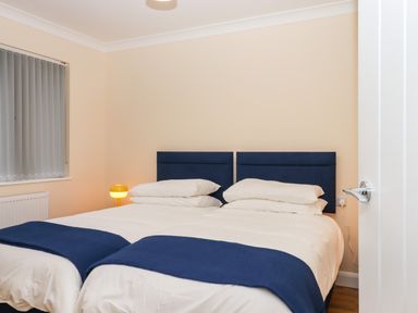 A bedroom with two single beds pushed together with blue headboards and bed throws and a yellow bedside lamp at West View in Northlew near Hatherleigh