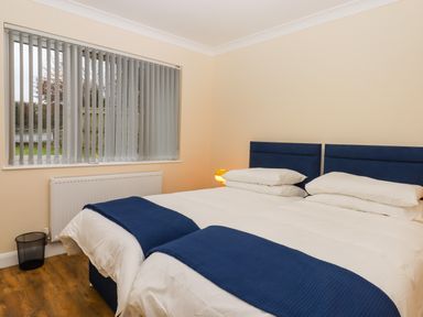 A bedroom with two beds with blue headboards and blue blankets near a window with vertical blinds at West View in Northlew near Hatherleigh
