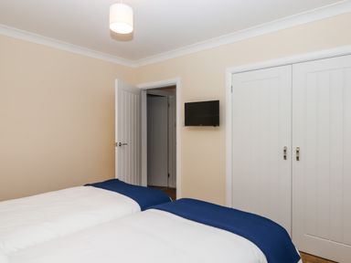 A bedroom with two beds covered in white and blue bedding a wall mounted television an open door and a closed wardrobe at West View in Northlew near Hatherleigh