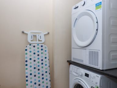 A laundry room with a stacked washer and dryer and an ironing board against the wall at West View in Northlew near Hatherleigh