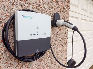 An electric vehicle charging station mounted on a pebble textured wall next to a white garage door at West View in Northlew near Hatherleigh