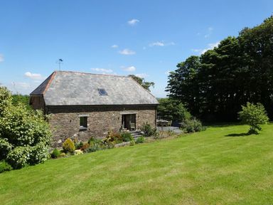 A stone house with a slate roof and a garden with bushes and a lawn at Swallows Reach in Halwell