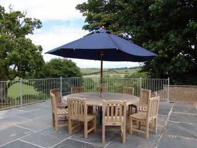 An outdoor patio with a round wooden table surrounded by wooden chairs and a large blue umbrella at Swallows Reach in Halwell