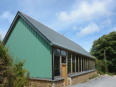 A building with green corrugated siding stone base and large windows at Swallows Reach in Halwell