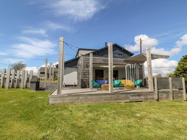 An outdoor wooden deck with chairs and pergola attached to a modern house with a grassy yard at Forest Lodge in Newborough