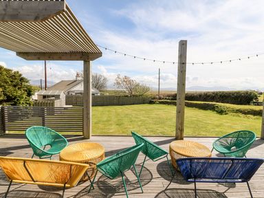 An outdoor patio with colorful chairs and tables overlooking a garden and a house in the distance at Forest Lodge in Newborough