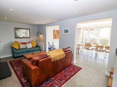 A living room with a brown leather sofa a teal fabric sofa a wooden coffee table and a dining area with chairs at Forest Lodge in Newborough