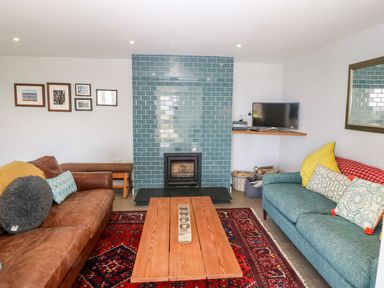 A living room with two sofas a wooden coffee table a red patterned rug a fireplace with blue tiles and a TV on a wall shelf at Forest Lodge in Newborough