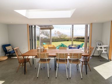 A dining area with a wooden table and chairs overlooking a garden with outdoor seating at Forest Lodge in Newborough