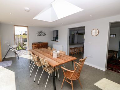 A dining room with a wooden table and chairs a high chair and a wall clock at Forest Lodge in Newborough
