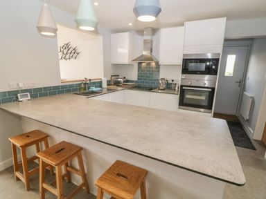 A kitchen with a large countertop and wooden stools with cabinets and appliances at Forest Lodge in Newborough