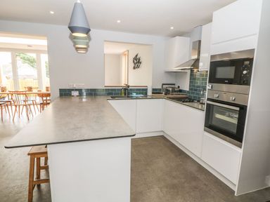 A kitchen with white cabinets a long countertop hanging lights and built in oven at Forest Lodge Newborough