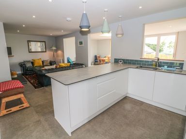 A kitchen with an island and hanging lights next to a living area with sofas at Forest Lodge in Newborough