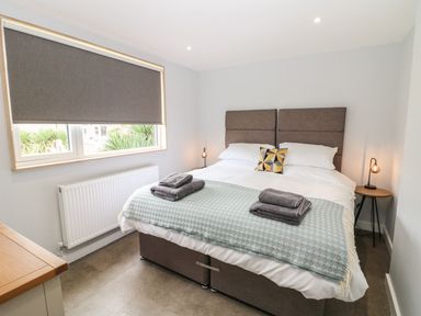 A bedroom with a double bed two folded towels on the bed a bedside table with a lamp and a window with a closed blind at Forest Lodge in Newborough