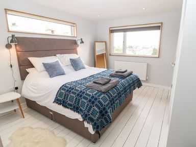 A bedroom with a double bed with pillows and folded towels by a window and a mirror at Forest Lodge in Newborough